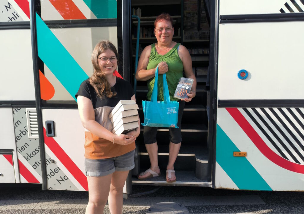 Zwei Einheimische stehen mit Büchern vor der Fahrbibliothek.