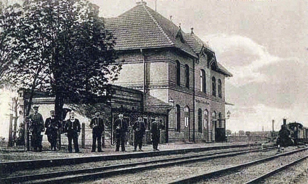 Zu sehen ist eine alte Aufnahme vom Bahnhof. In dem Augenblick fährt gerade eine Dampflokomotive ein.